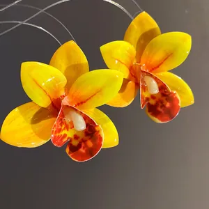 Primo piano di orecchini a perno a forma di orchidea in resina gialla con finitura lucida.