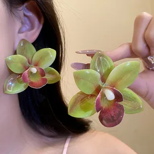 Dettaglio degli orecchini a forma di orchidea con petali in resina traslucida verde e rossa.