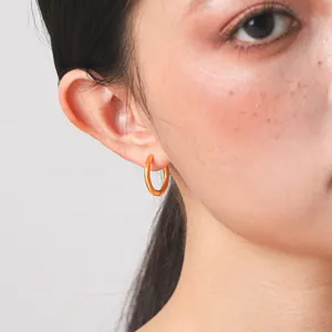 Macro view of a minimalist gold titanium steel hoop earring worn on a female model's ear.