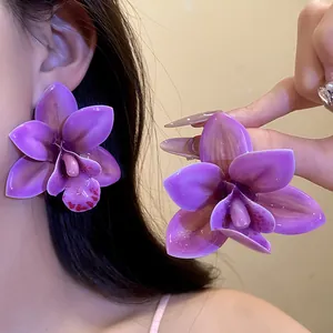 Primo piano di orecchini a forma di orchidea viola indossati e tenuti in mano