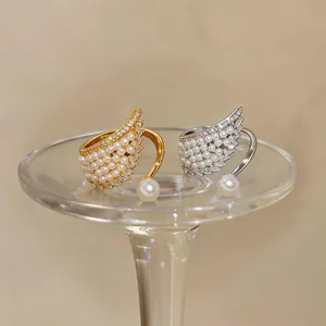 Detailed view of elegant gold and silver wing-shaped rings with pearls and sparkling zircons