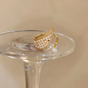 Macro view of a gold wing-shaped open ring featuring inlaid pearls and zircons