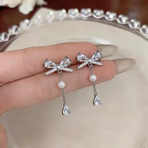 Elegant silver bow stud earrings with sparkling zircons and dangling white pearls.