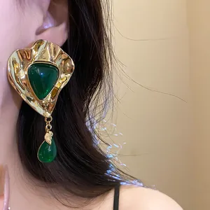 Detail view of vintage-style gold earrings with emerald green resin teardrop charms