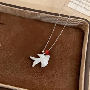 Macro view of elegant white shell swallow pendant necklace with red bead detail