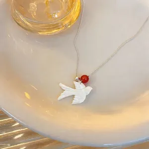 Close-up of a minimalist white shell swallow necklace with an elegant red bead.