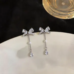 Detail view of silver bow earrings featuring sparkling zircons and delicate pearl drops.