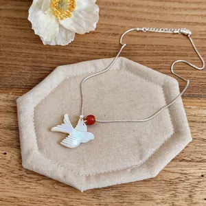 Detailed view of a shell swallow pendant necklace with a red bead on a wooden background.