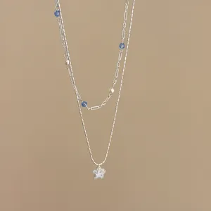 Detail view of a double-layered silver necklace with zirconia star and blue beads.