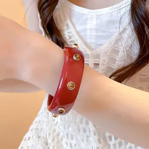 Bracelet jonc rétro en résine rouge avec des accents de clous dorés porté au poignet