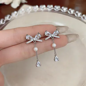 Detailed close-up of elegant silver bow-knot earrings with zircon and pearl tassels