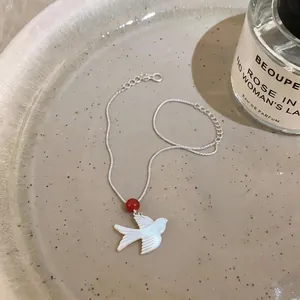 Detailed shot of a shell swallow bird pendant on a silver necklace with a red bead.