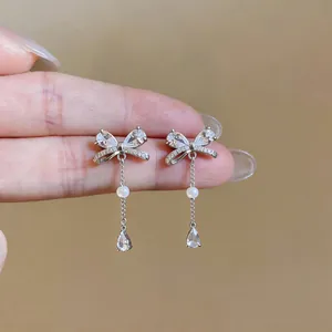 Macro view of silver bow-shaped earrings featuring sparkling zircon and dangling pearls