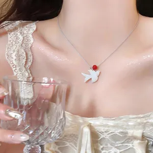 Close-up of a shell swallow pendant necklace with a red bead worn by a female model