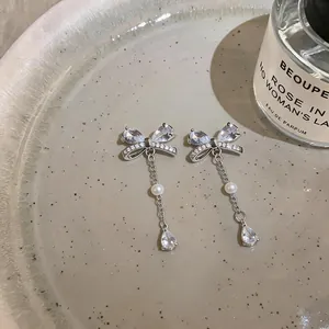 Close-up of bow earrings with shimmering zirconia and elegant pearl drops on a ceramic plate.