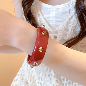 Bracelet jonc en résine rouge vintage avec rivets dorés et pierres brunes au poignet