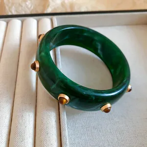Gros plan d'un bracelet en résine verte vintage avec rivets dorés et pierres d'œil de tigre