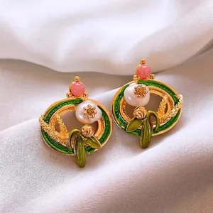 Detailed macro view of vintage floral enamel pearl stud earrings on white silk background