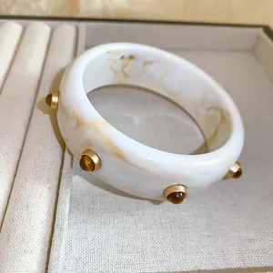 Gros plan sur un bracelet en résine vintage avec marbrure ambre et clous dorés élégants.