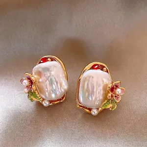 Close-up of artistic Baroque pearl earrings with floral enamel and gold frame details