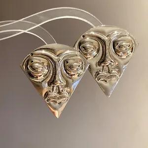Detailed macro view of vintage silver human face relief earrings in a unique triangle shape