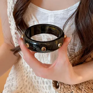 Détail d'un bracelet vintage en résine marbrée foncée avec des clous dorés par un mannequin