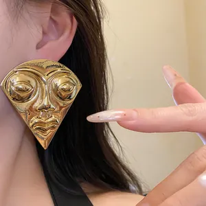 Detail view of exaggerated gold fan-shaped mask earring with an artistic portrait