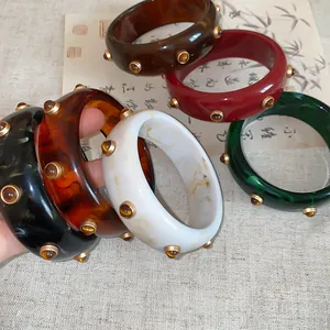 Une collection de bracelets rétro en résine avec des rivets dorés en plusieurs couleurs