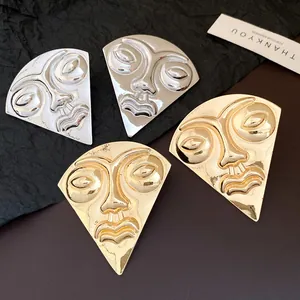 Detailed macro view of abstract human face fan-shaped stud earrings in gold and silver metal