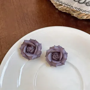 Primo piano di orecchini a forma di rosa viola su un piatto di ceramica bianca