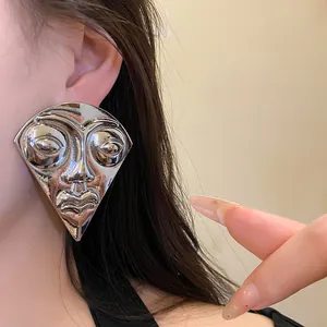 Close-up of oversized silver-tone fan-shaped earring with retro human face design