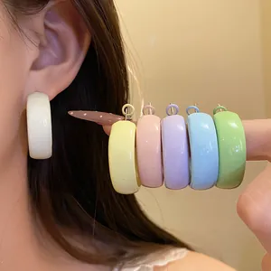 Detailed close-up of vibrant C-shaped pastel hoop earrings in multiple colors shown on hand