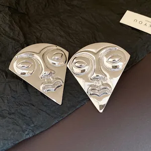 Close-up of vintage silver fan-shaped face mask stud earrings on textured background
