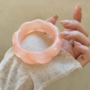 Dettaglio macro di un bracciale geometrico in acrilico rosa ondulato in stile vintage.