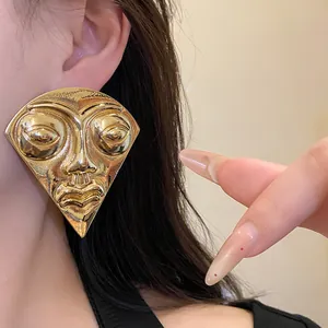 Detailed view of large golden fan-shaped earrings with abstract face portrait design