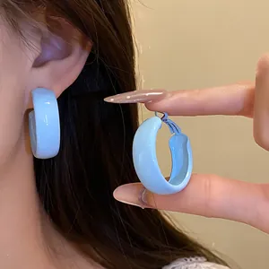 Detail of light blue painted hoop earrings shown worn on ear and held by fingers