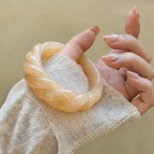 Dettaglio di un bracciale rigido in acrilico intrecciato retrò con trama cremosa elegante