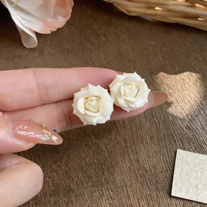 Dettaglio macro di orecchini a rosa bianca placcati in oro 18 carati tenuti su un dito