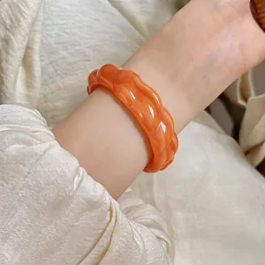 Dettaglio ravvicinato di un bracciale a cerchio in acrilico arancione intrecciato su un polso