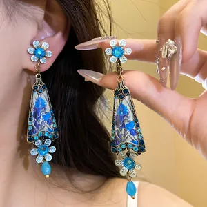 Macro detail of vintage court style earrings with blue floral patterns and rhinestones.