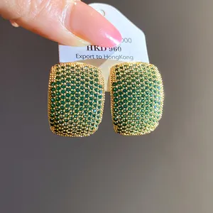 Detailed macro view of vintage gold-plated C-shaped earrings encrusted with green zircons
