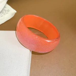 Detailed view of a wide orange resin bangle with a shimmering glitter finish and smooth texture