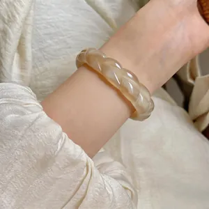 Vista dettagliata di un bracciale in acrilico intrecciato crema sul polso di una donna.
