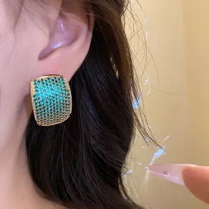 Close-up detail of vintage gold-tone C-shaped earrings paved with teal zircons on ear