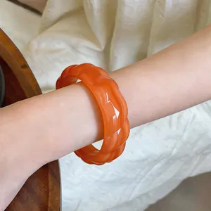 Primo piano che mostra la trama lucida del bracciale rigido in acrilico arancione