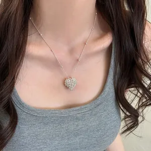 Macro view of a delicate silver heart pendant necklace worn on a model's neckline
