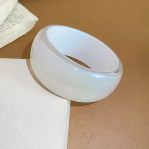 Close-up of white iridescent resin bangle with shimmer on a textured display box.