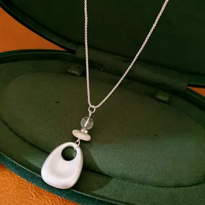 Detailed shot of a geometric stone and matte silver pendant on a delicate sweater chain