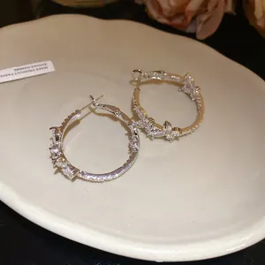 Macro detail of 18k gold-plated zircon butterfly hoop earrings with sparkling silver needles