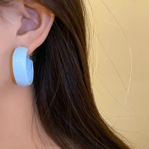 Close-up of a light blue spray-painted C-shaped hoop earring worn by a female model